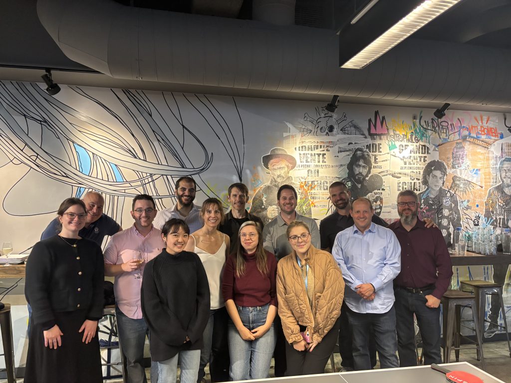 Team posing together indoors behind a ping pong table in front of a colorful graffiti wall.